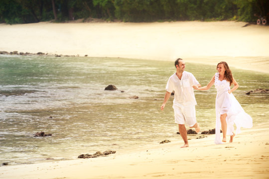 bride and groom run barefoot on sandy beach