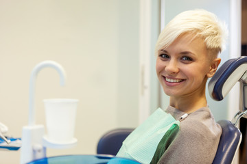 Blonde smiling woman sitting at the dentist and looking towards