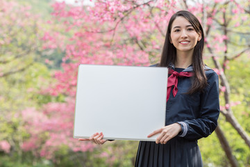 桜をバックにホワイトボードを持つ女子学生