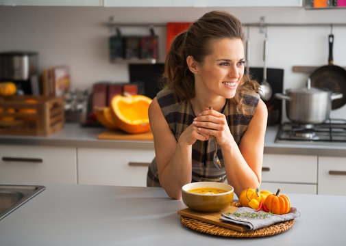 Young housewife eating pumpkin soup in kitchen