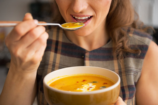 Closeup on young woman eating pumpkin soup in kitchen