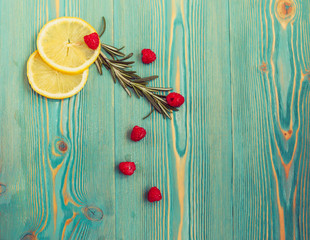 lemon slices, raspberry and rosemary on turquoise wooden desk