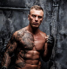 Muscular strong male with tattoo poses over the wall