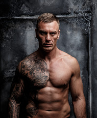 Fototapeta na wymiar Muscular strong male with tattoo poses over the wall