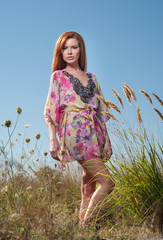 Beautiful young woman in wild flowers field over blue sky