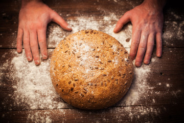 Baker hands with fresh bread on table