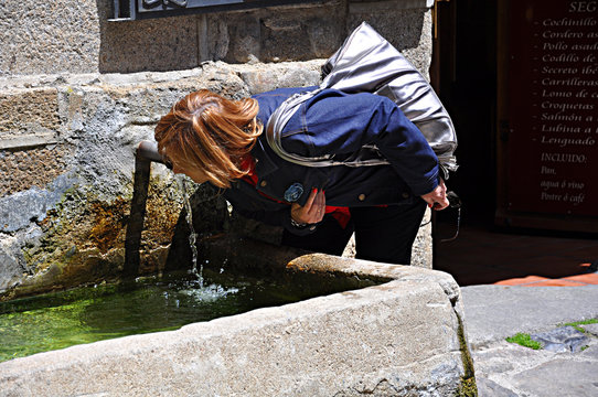 Mujer bebiendo agua de una fuente pública