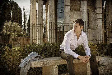 Handsome young man in European city, sitting on stone bench