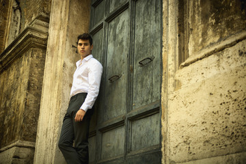 Elegant young man leaning against old wall and door