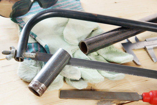 Composition with hacksaw and metal pipe on the wooden workbench