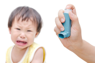 Woman's hand holding asthma inhaler foreground and crying baby s