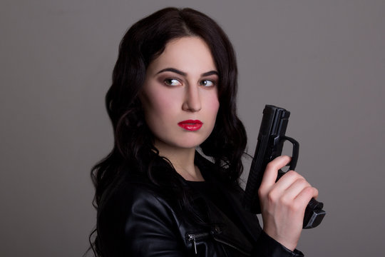portrait of young beautiful woman with gun over grey