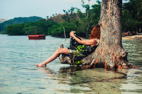 Woman sitting up against tree on tropical beach