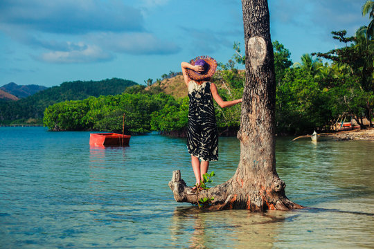 Woman with hat by tree on tropical beach