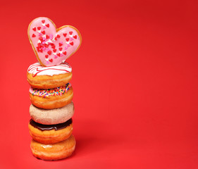 Sweet donuts with heart shaped donut on the top over red