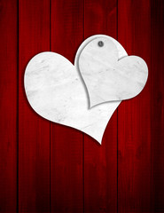 Conceptual two white old paper vintage hearts on red wood