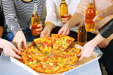 Friends hands with bottles of beer and pizza, close up