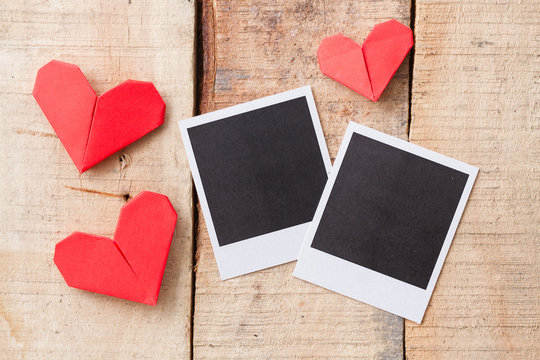Instant photos with origami hearts. On wooden background