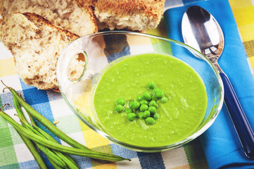 Green pea soup in a transparent bowl on a colorful tablecloth.