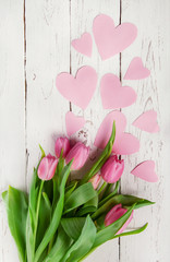 Pink tulips bouquet with paper hearts on wooden background