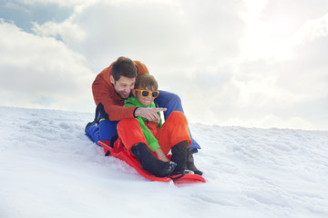 Fototapeta na wymiar father and son having fun in the snow, sliding