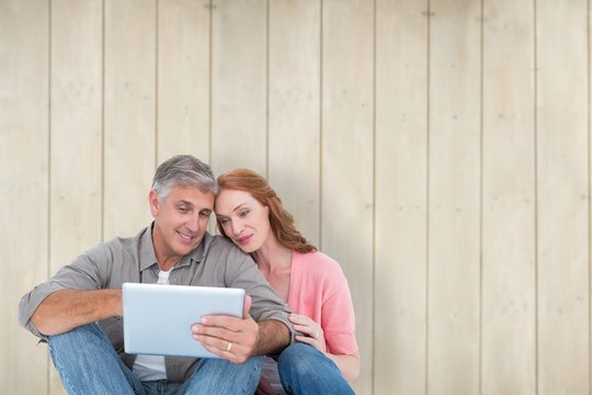 Composite image of casual couple sitting using tablet