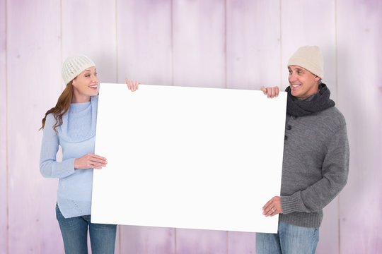 Composite image of casual couple in warm clothing holding poster