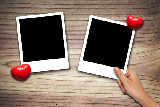 hand placing Blank valentine photo frames on wood background