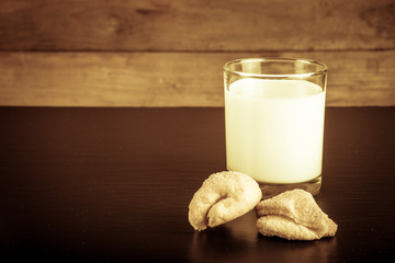 Two cookies and glass of milk on a black table against old woode