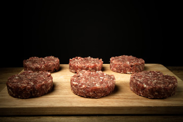 Raw cutlet of minced meat on a wooden cutting board on black bac