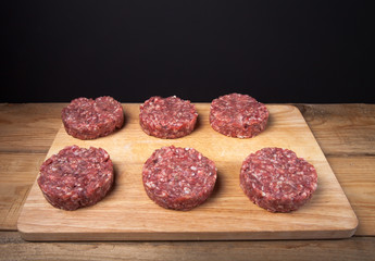 Raw cutlet of minced meat on a wooden cutting board on black bac