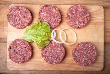Raw cutlet of minced meat with leaf of salad and rings of onion