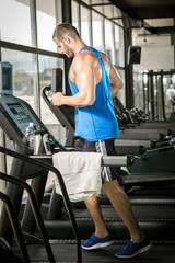 Fototapeta na wymiar Young man running at treadmill in gym