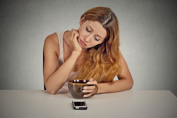 Sad woman sitting at table looking at mobile phone