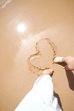 Junges verliebtes Paar malt Herz in den Sand