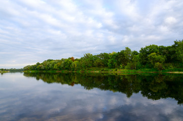 Trees on bank of pond and clouds are reflecting in water