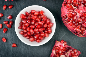 Red pomegranate seeds in a white bowl on table. 