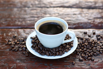 Black coffee in the cup on old wood table with coffee beans