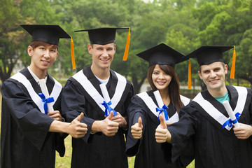 happy students in graduation gowns showing diplomas with thumbs