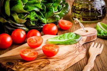 cherry tomatoes on olive cutting board with green lettuce