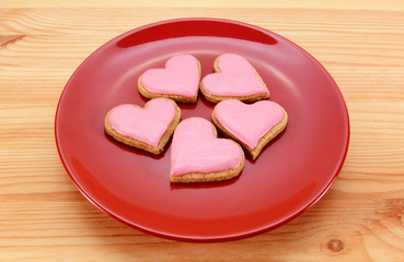 Five heart-shaped iced cookies on a red plate