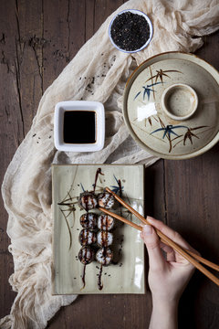 overhead shot of hands with chopstick taking sushi from plate