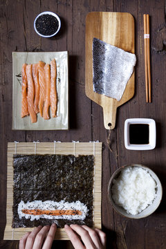overhead shot of hands rolling sushi and ingredients on table