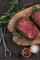 Raw peppered steak with herbs on wooden table