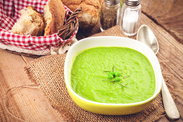 Green pea soup in a bowl with bread and sour cream on rustic lin