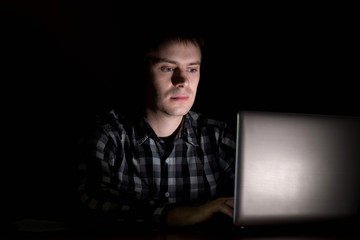 Young man sitting at a laptop in the dark