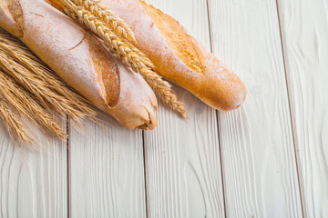 two baguettes and ears of wheat on old white wooden boards with