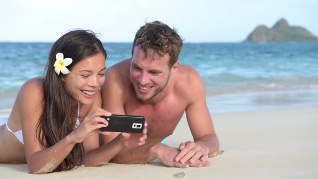 Beach holiday couple using smartphone fun laughing