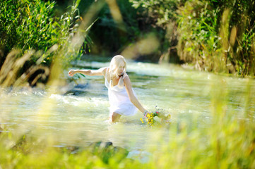 girl in a white sundress on the river starts a wreath of flowers