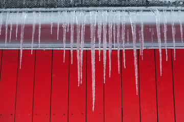 Icicles on the roof. Red wooden background.